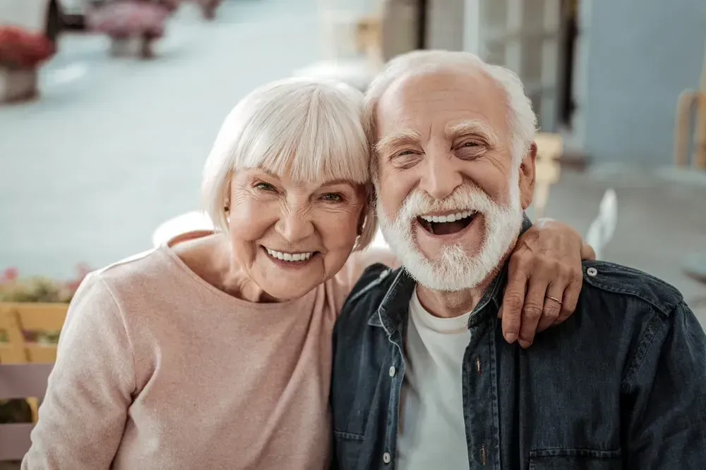 A Man and a Woman Are Posing for a Picture and Smiling for the Camera — Twin Towns Denture Clinic In Forster, NSW