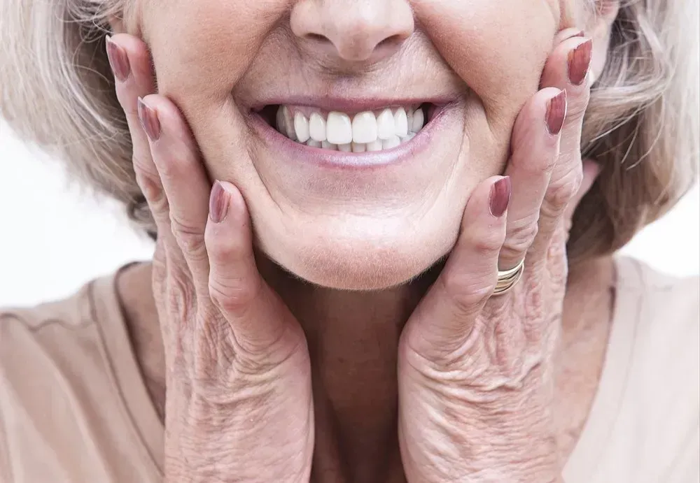 An Elderly Woman is Smiling With Her Hands on Her Face — Twin Towns Denture Clinic In Forster, NSW