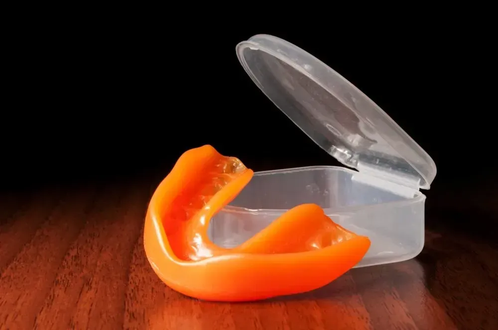 An Orange Mouth Guard is Sitting in a Plastic Case on a Wooden Table — Twin Towns Denture Clinic In Forster, NSW