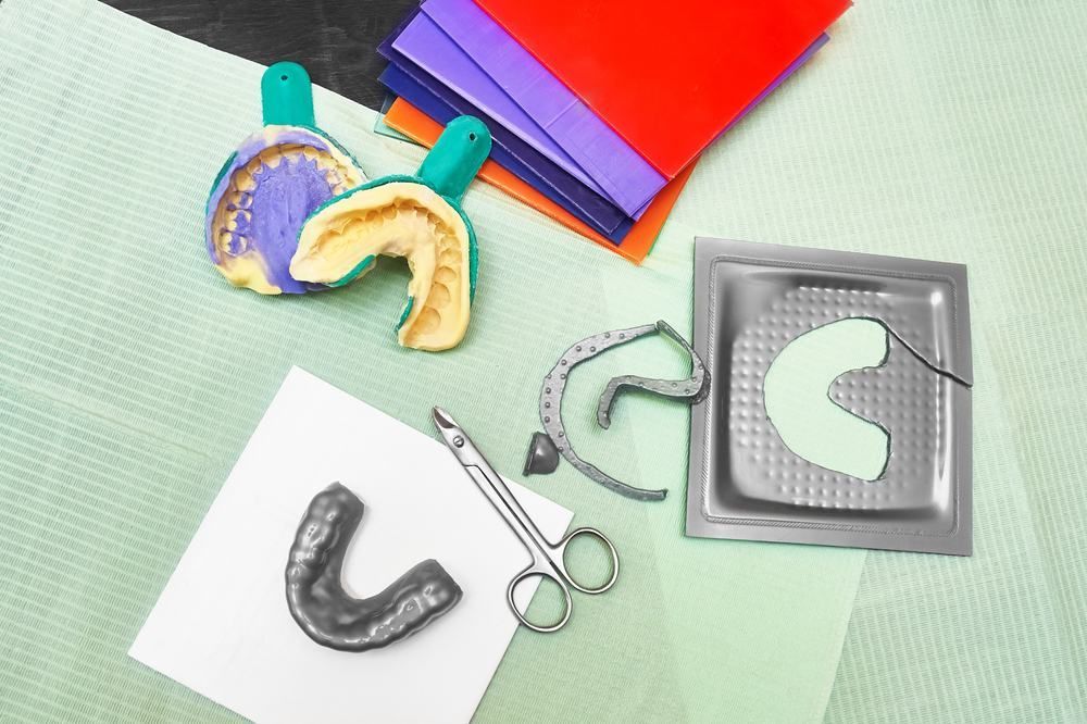 A Dental Tray, a Pair of Scissors, and a Dental Mouthguard on a Table — Twin Towns Denture Clinic In Forster, NSW
