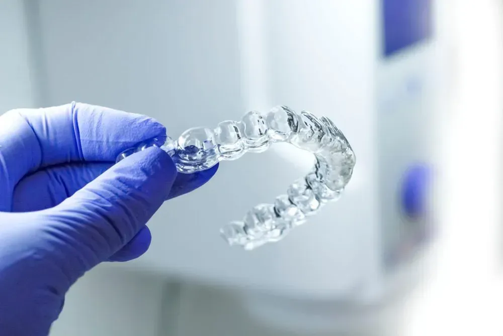 A Person Wearing Blue Gloves is Holding a Clear Brace in Their Hand — Twin Towns Denture Clinic In Laurieton, NSW