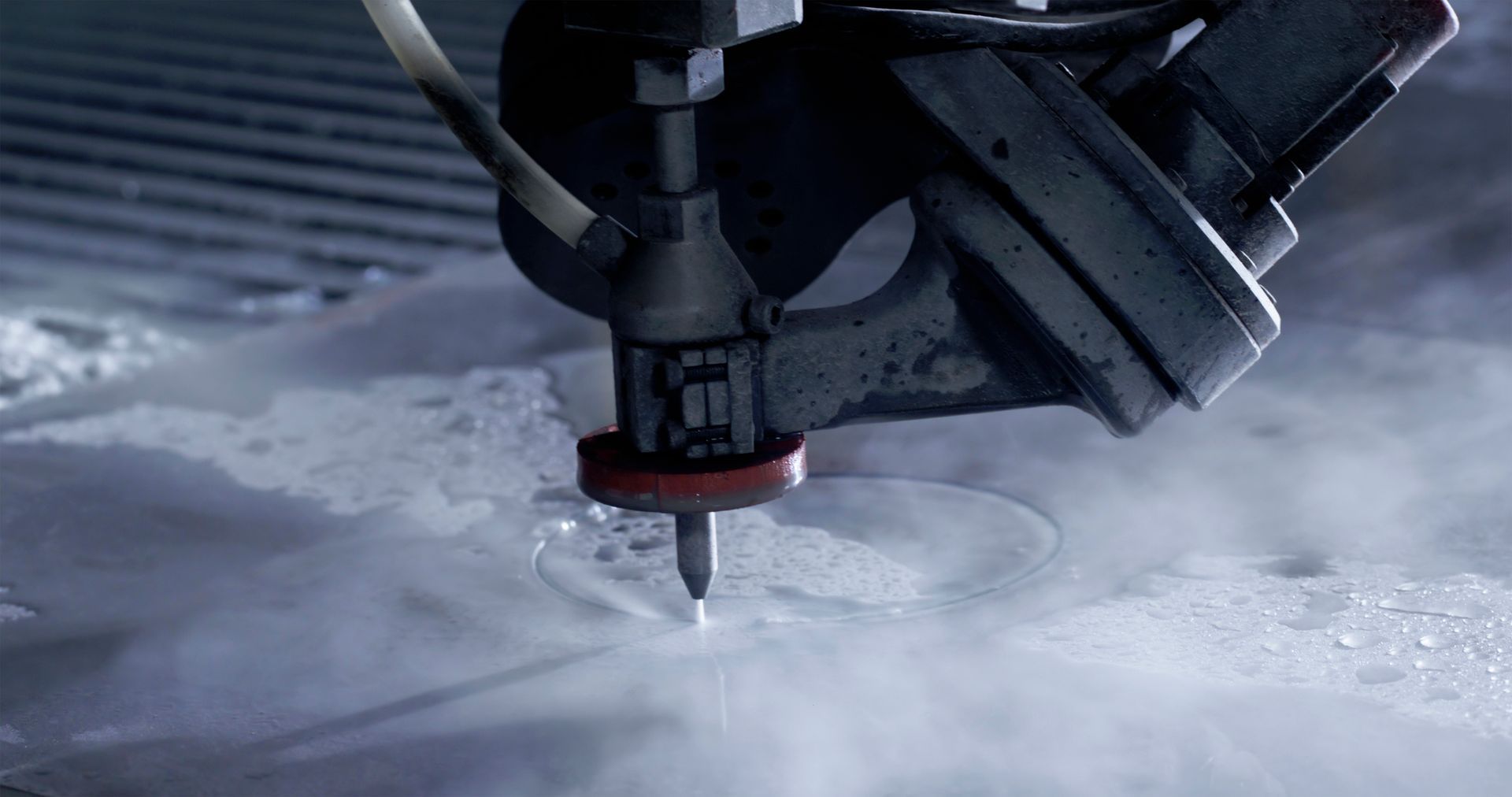 Water jet cutter cutting a circular shape in a metal sheet, producing vapor.