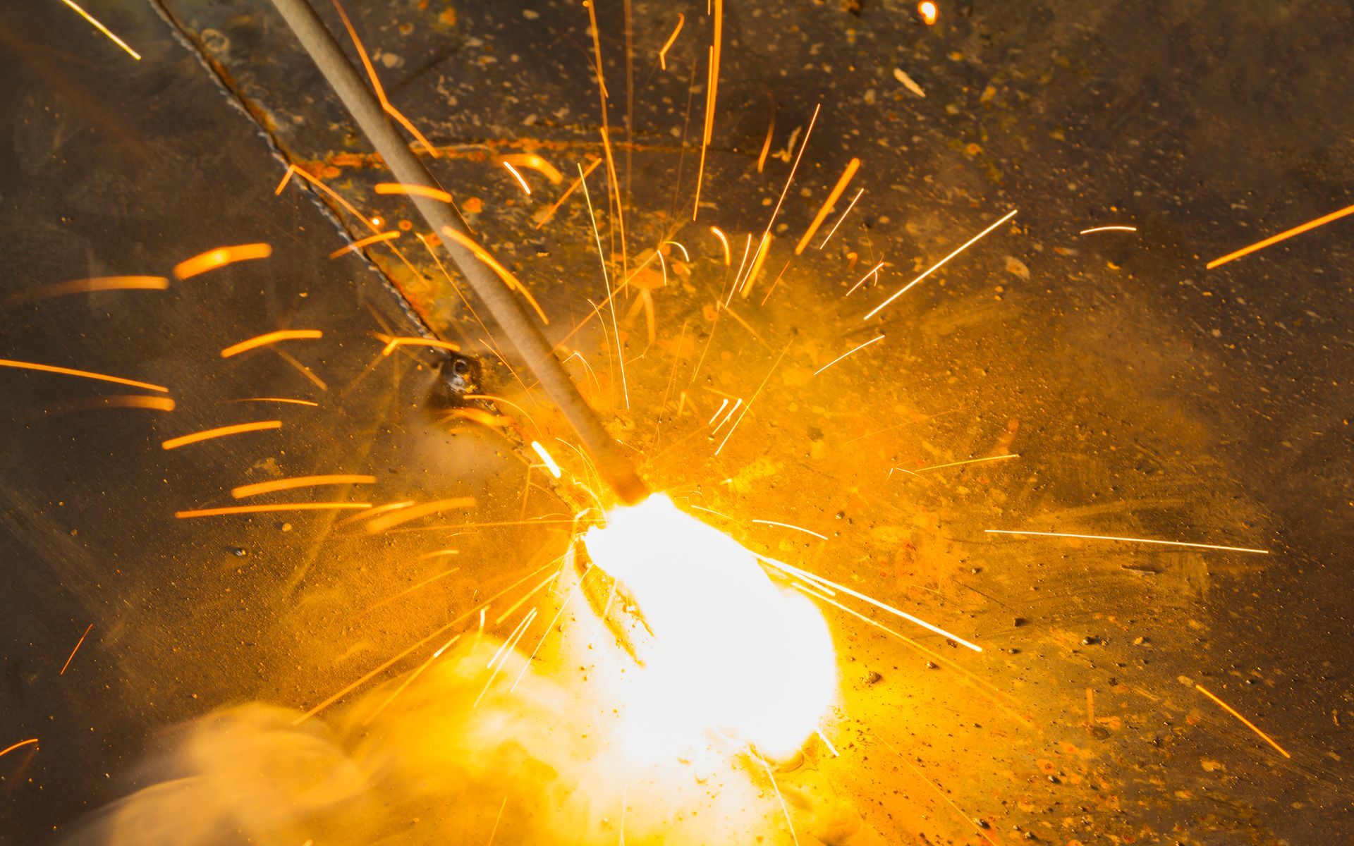 Welding sparks flying from a metal rod during the welding process. Bright orange and yellow colors.