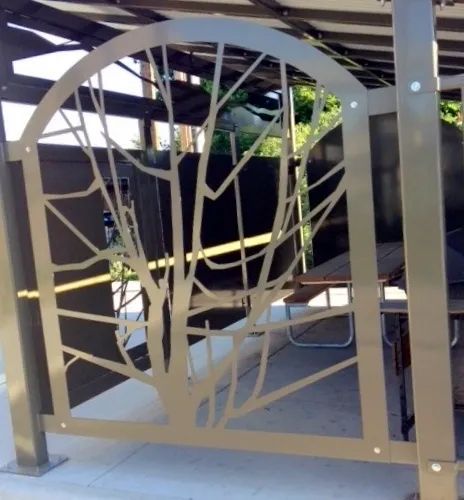 Metal gate with tree design, arching at the top, installed in a covered outdoor area.