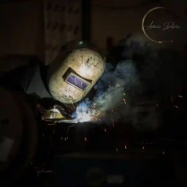 Welder in a protective mask welding metal; sparks and smoke are visible.
