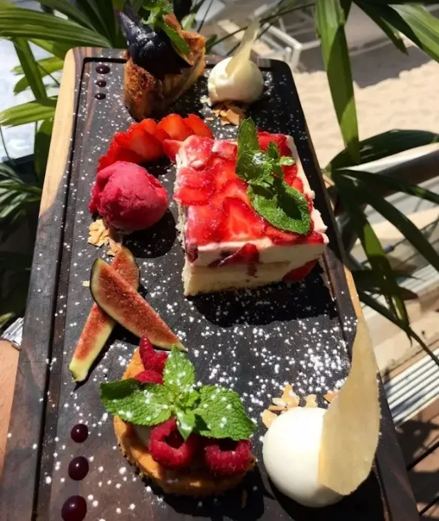 Plateau de desserts avec gâteau, fruits, glace et menthe sur une planche en bois.
