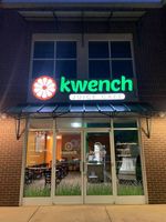 Kwench storefront at night with glowing green sign and glass doors