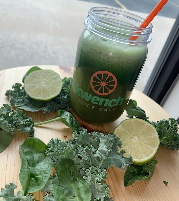 Green juice in a glass jar with orange straw, surrounded by lime halves and kale leaves on a table
