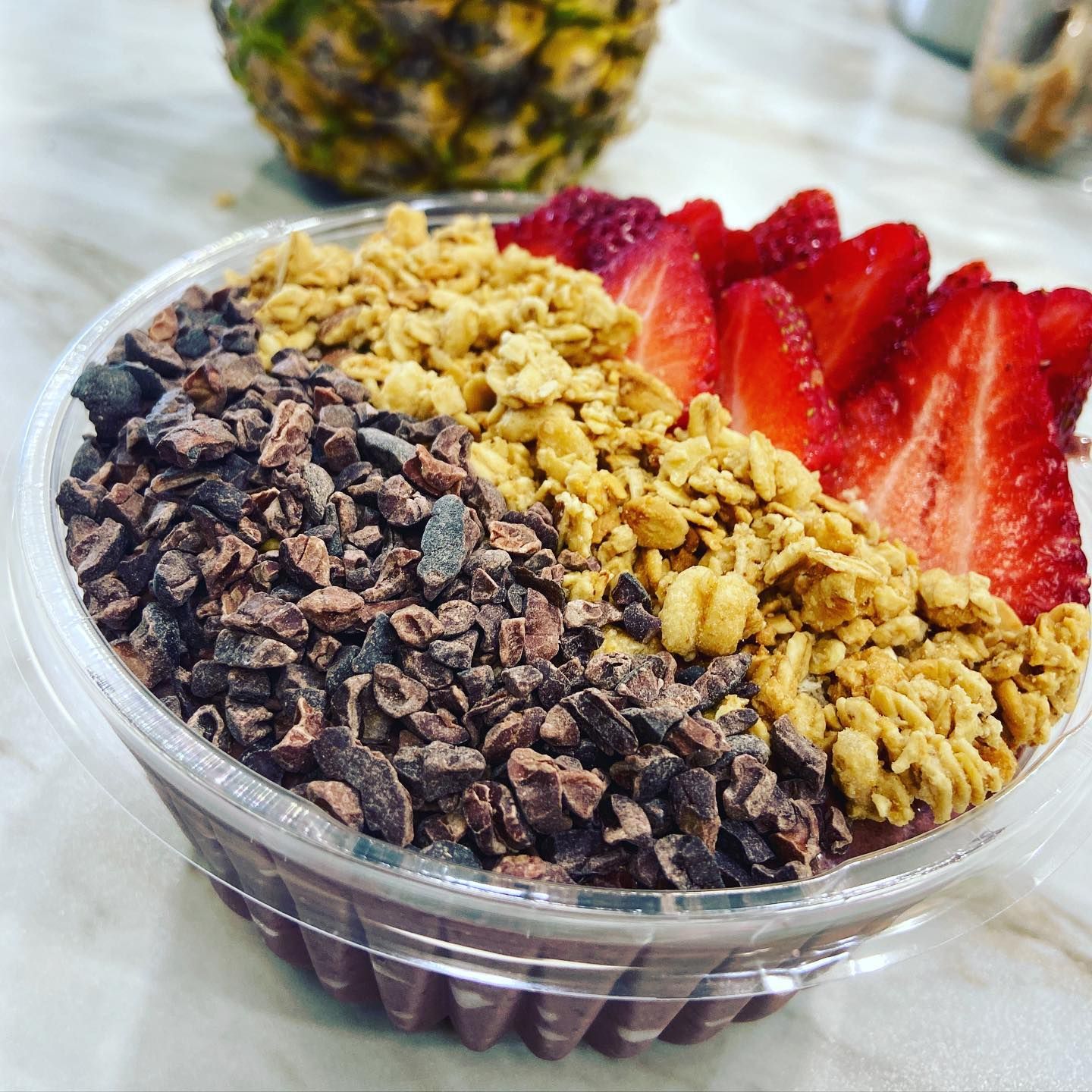 Chocolate açaí bowl topped with granola, cacao nibs, and sliced strawberries in a plastic cup