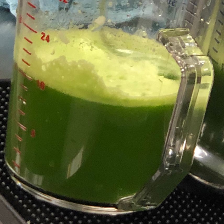 A blender jar filled with bright green liquid and frothy foam on top