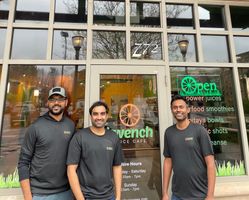 Three people standing outside a storefront with green “Open” signage, smiling at the camera.