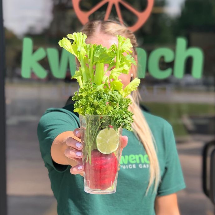 Person holding a red drink with mint, lime, and celery in front of a restaurant window