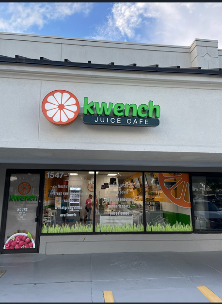 Storefront of Kwench Juice Cafe with green and orange sign on a white building