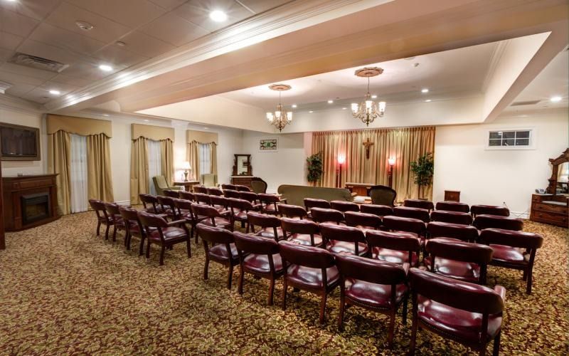 Empty banquet hall with rows of burgundy chairs facing a small stage and podium.