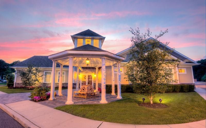 Elegant suburban home at dusk with a lit gazebo, pink sunset sky, and manicured lawn