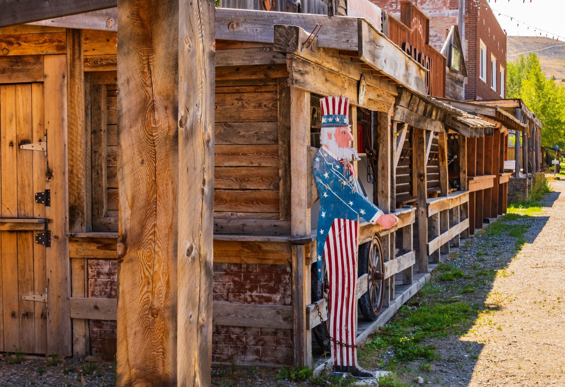 Uncle Sam cutout stands near a weathered wooden building with a walkway, in an outdoor setting.