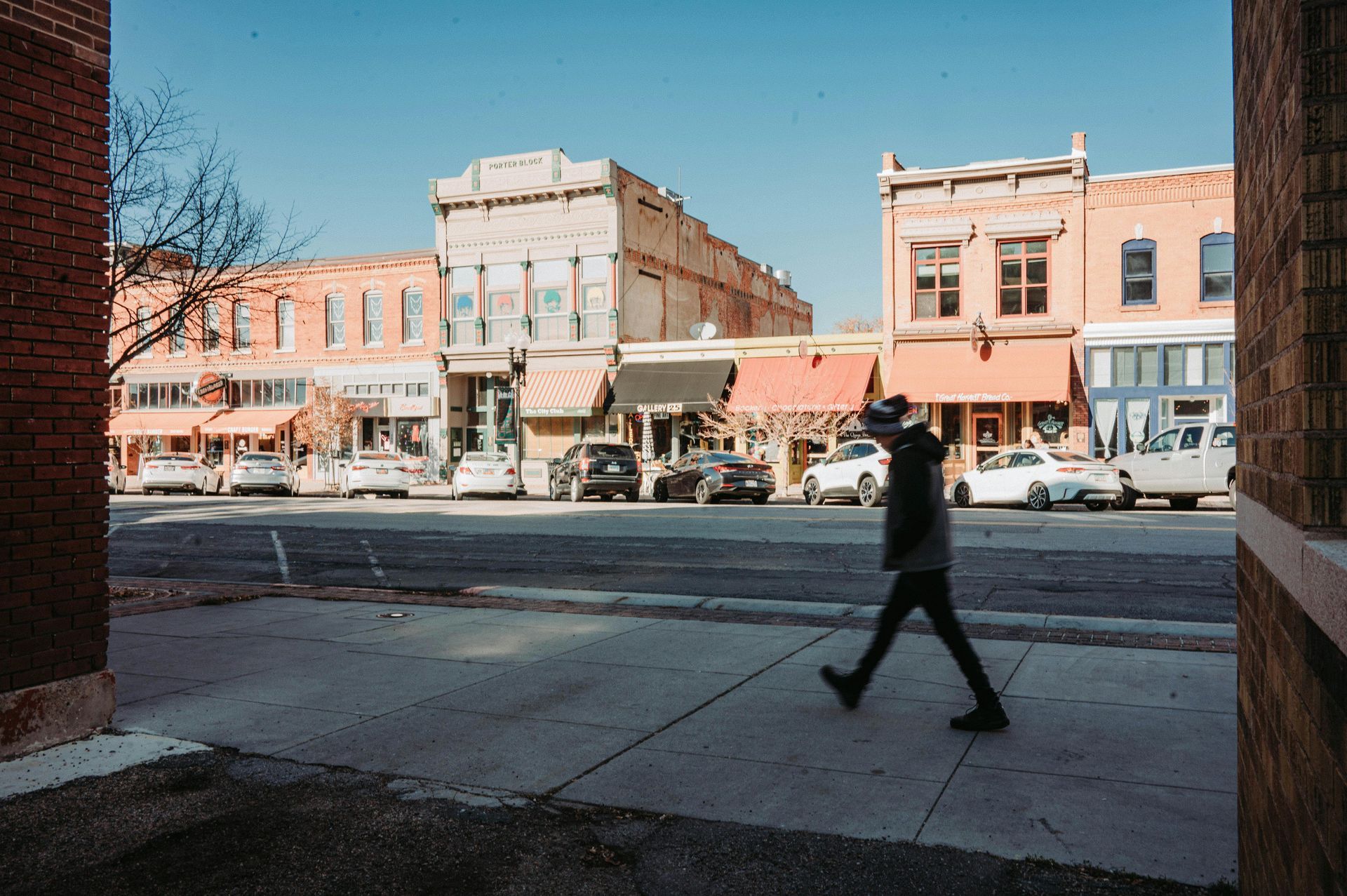Small-town street with brick storefronts and a person walking across the road in the foreground | City Realtor Springfield MO
