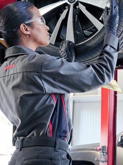Mecánico inspeccionando una rueda de coche en un elevador hidráulico en un taller de reparación.