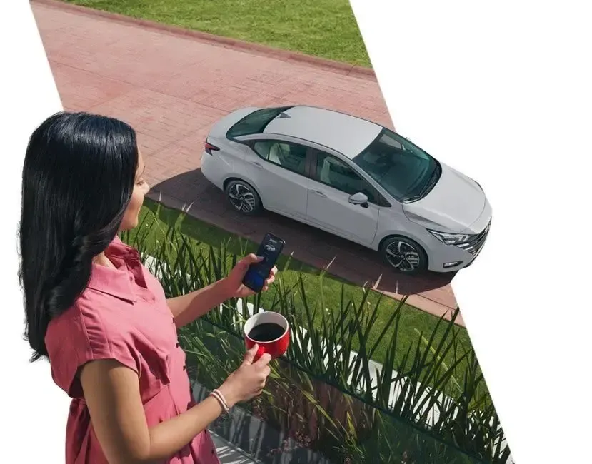 Mujer con un teléfono y una taza de café observa desde un balcón un coche plateado estacionado frente a una casa.