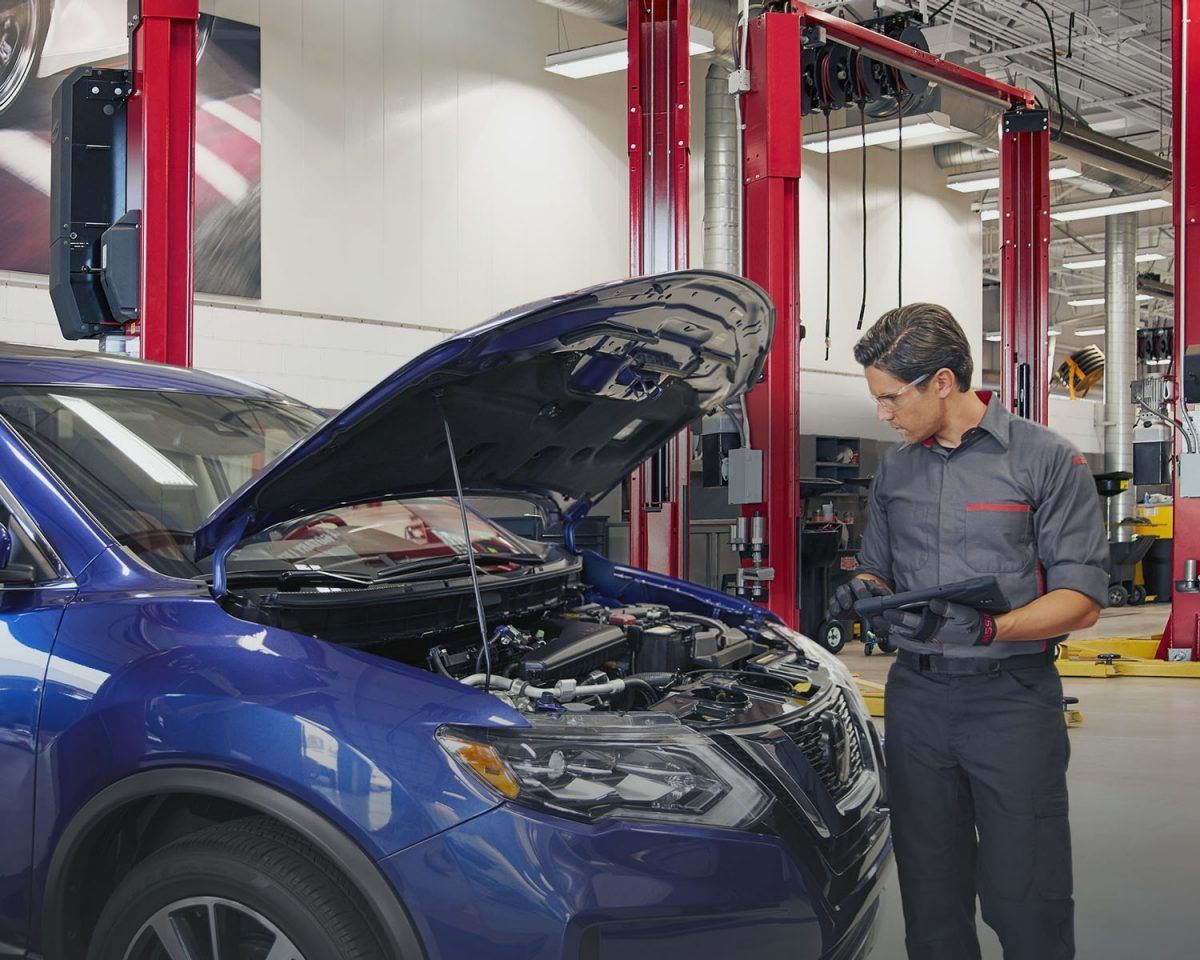 Un SUV azul en un taller con el capó abierto mientras un mecánico inspecciona el motor.