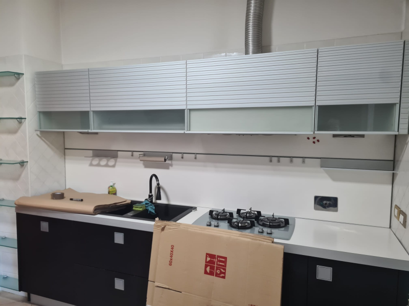 Cucina moderna con mobili grigi, lavello, piano cottura a gas e mobili base neri durante l'installazione
