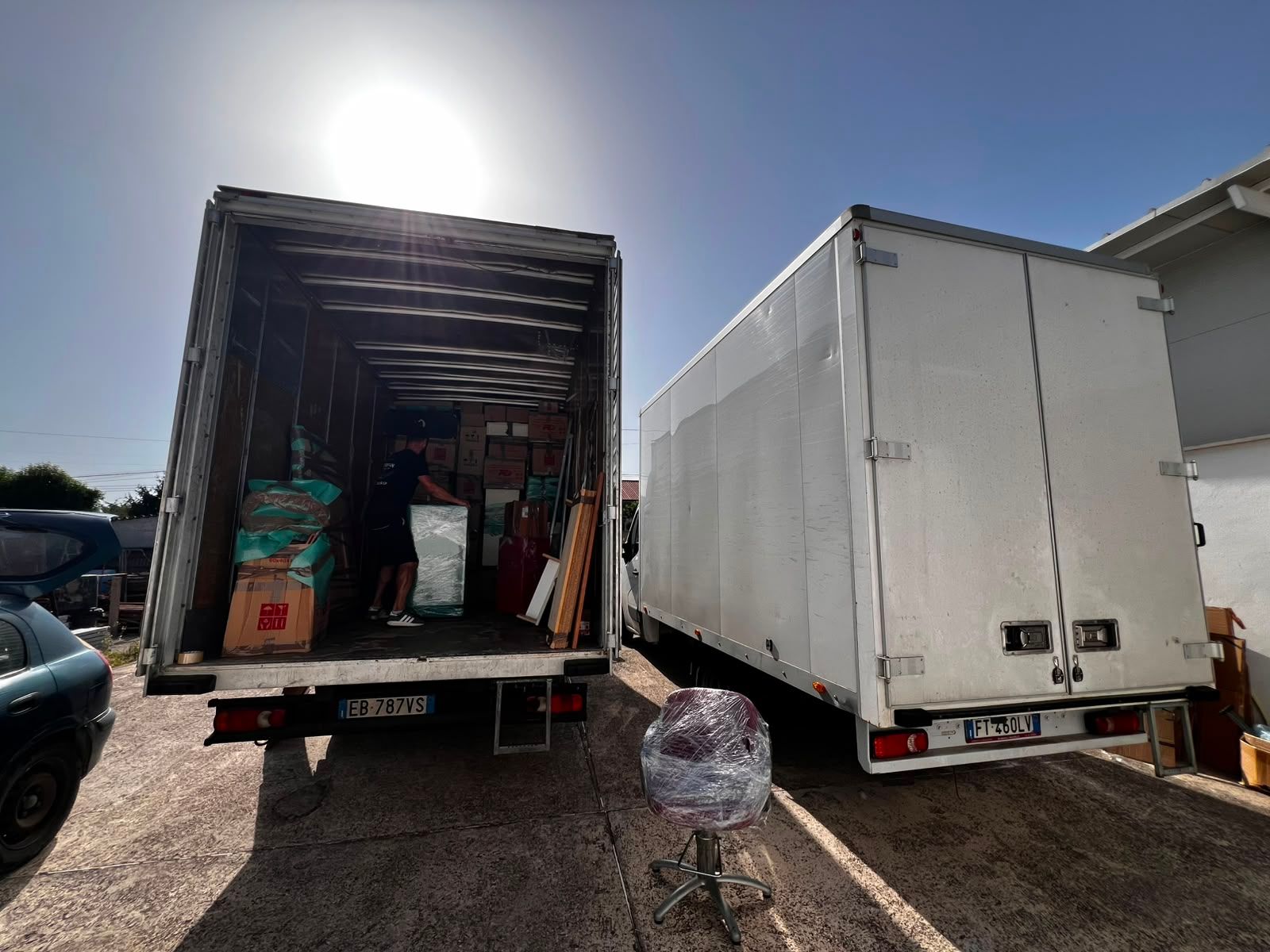 Due furgoni parcheggiati fianco a fianco, uno aperto con il carico all'interno, in un parcheggio soleggiato.