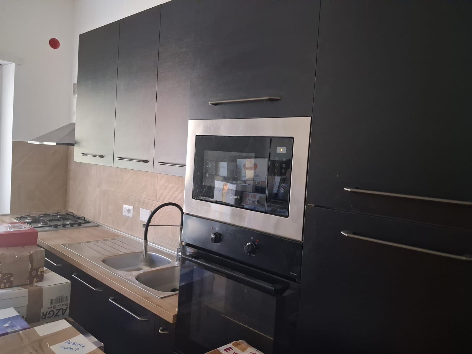 Cucina moderna con mobili scuri, forno a incasso, lavello e piano cottura a gas.