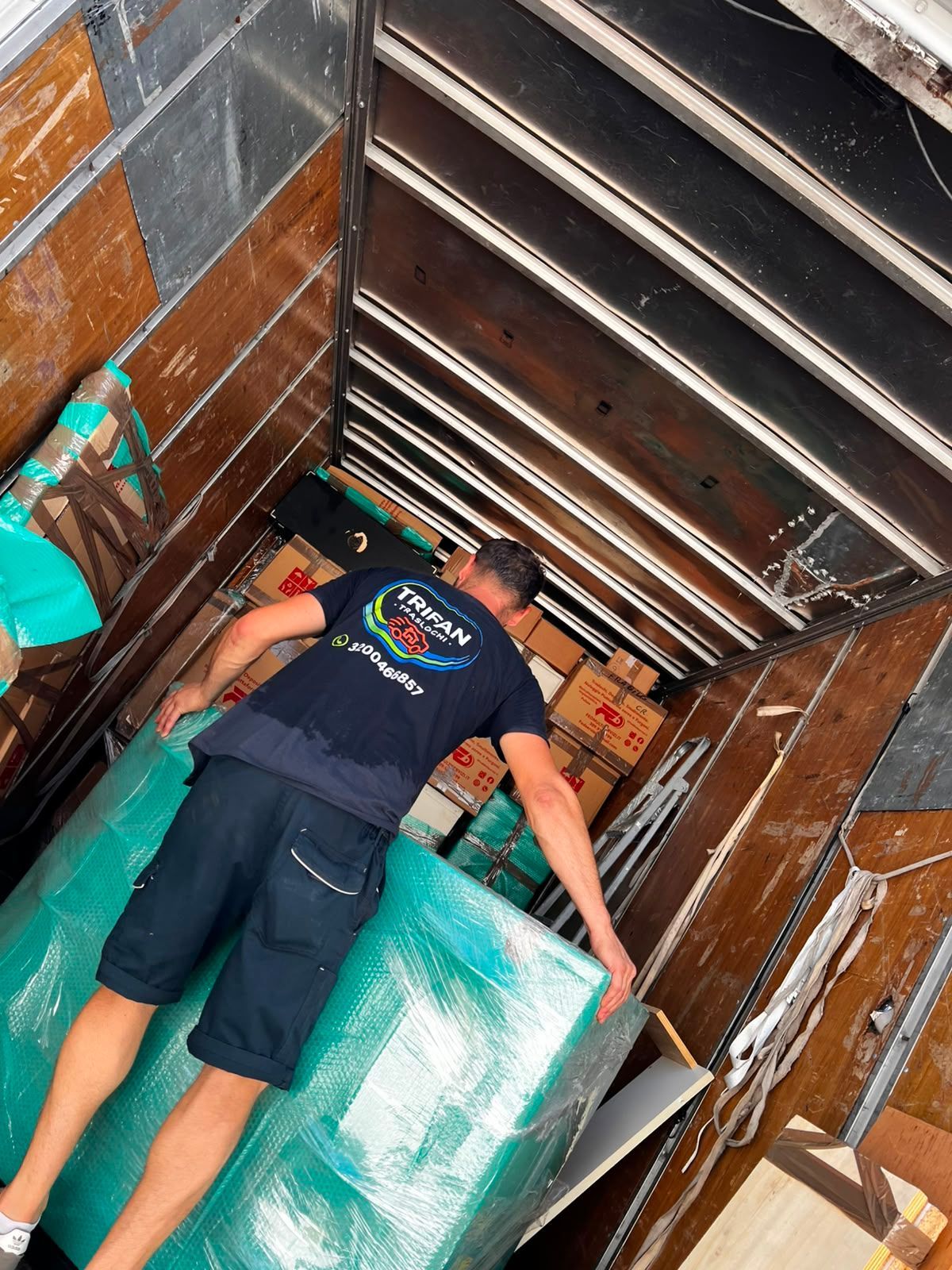 Una persona carica un grande pacco avvolto all'interno di un camion, insieme a scatole impilate.