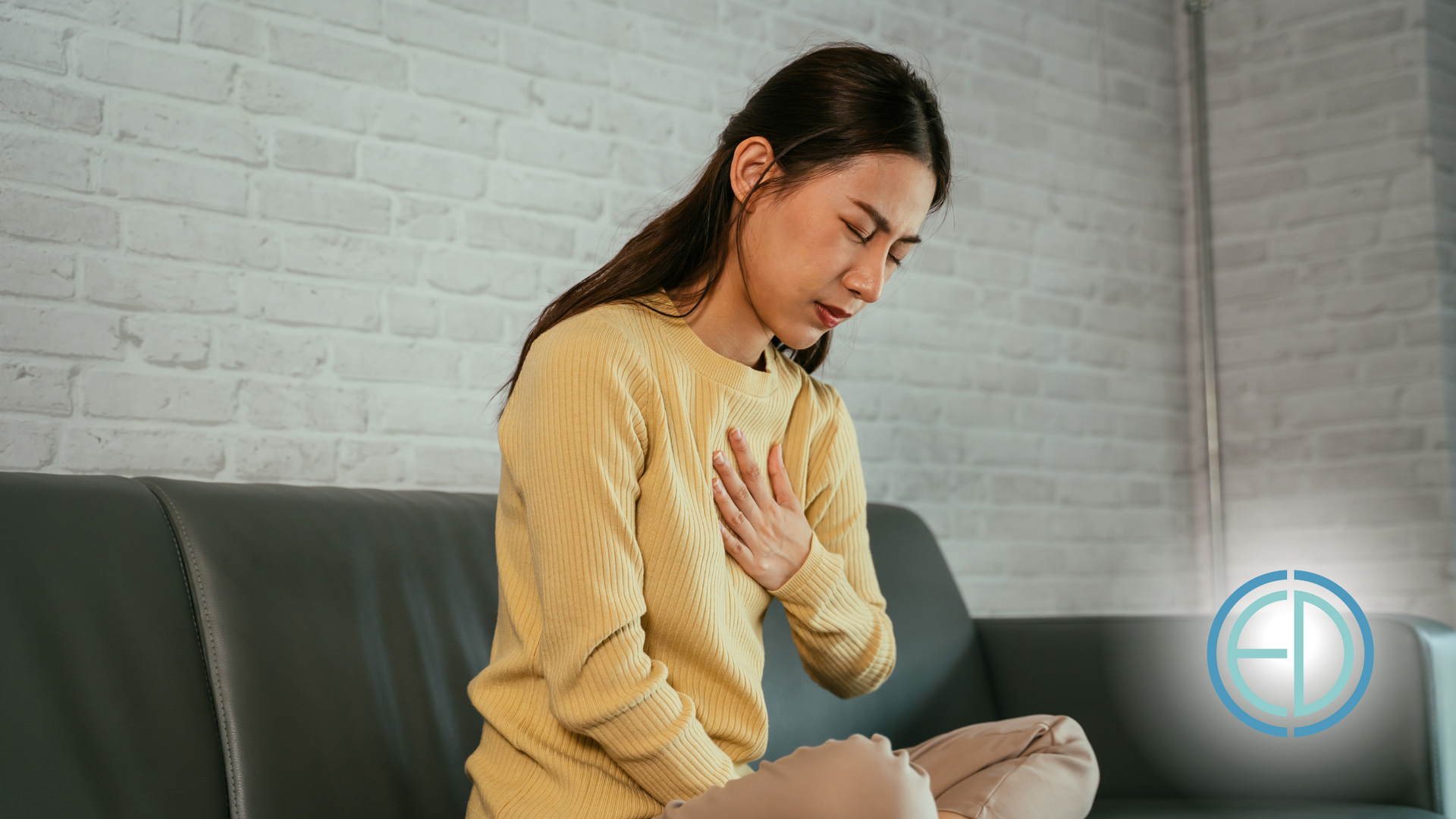 A woman is sitting on a couch with her hands on her chest.