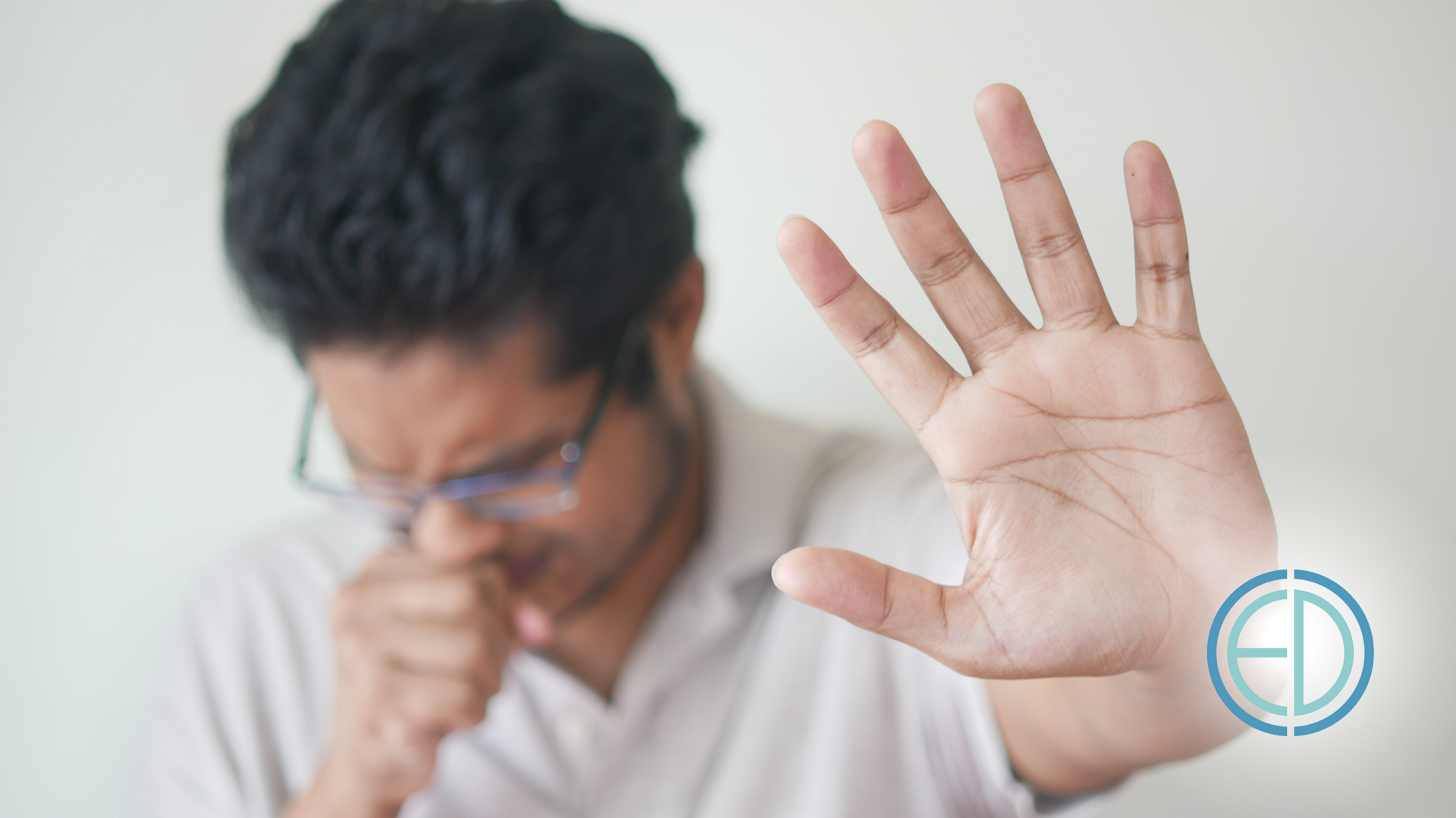 A man with glasses is coughing and making a stop sign with his hand