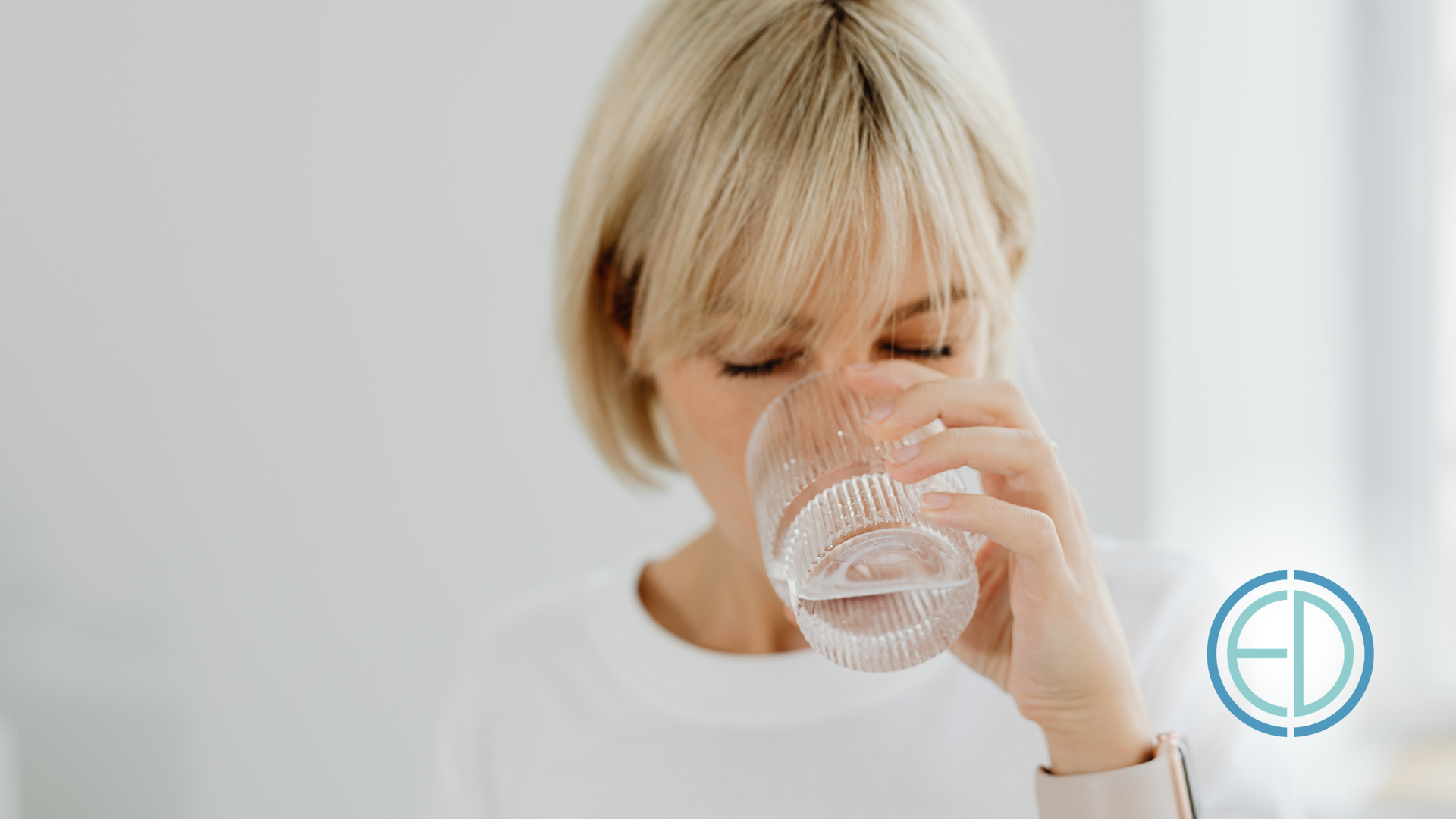 Person drinking water from a glass in a bright white room