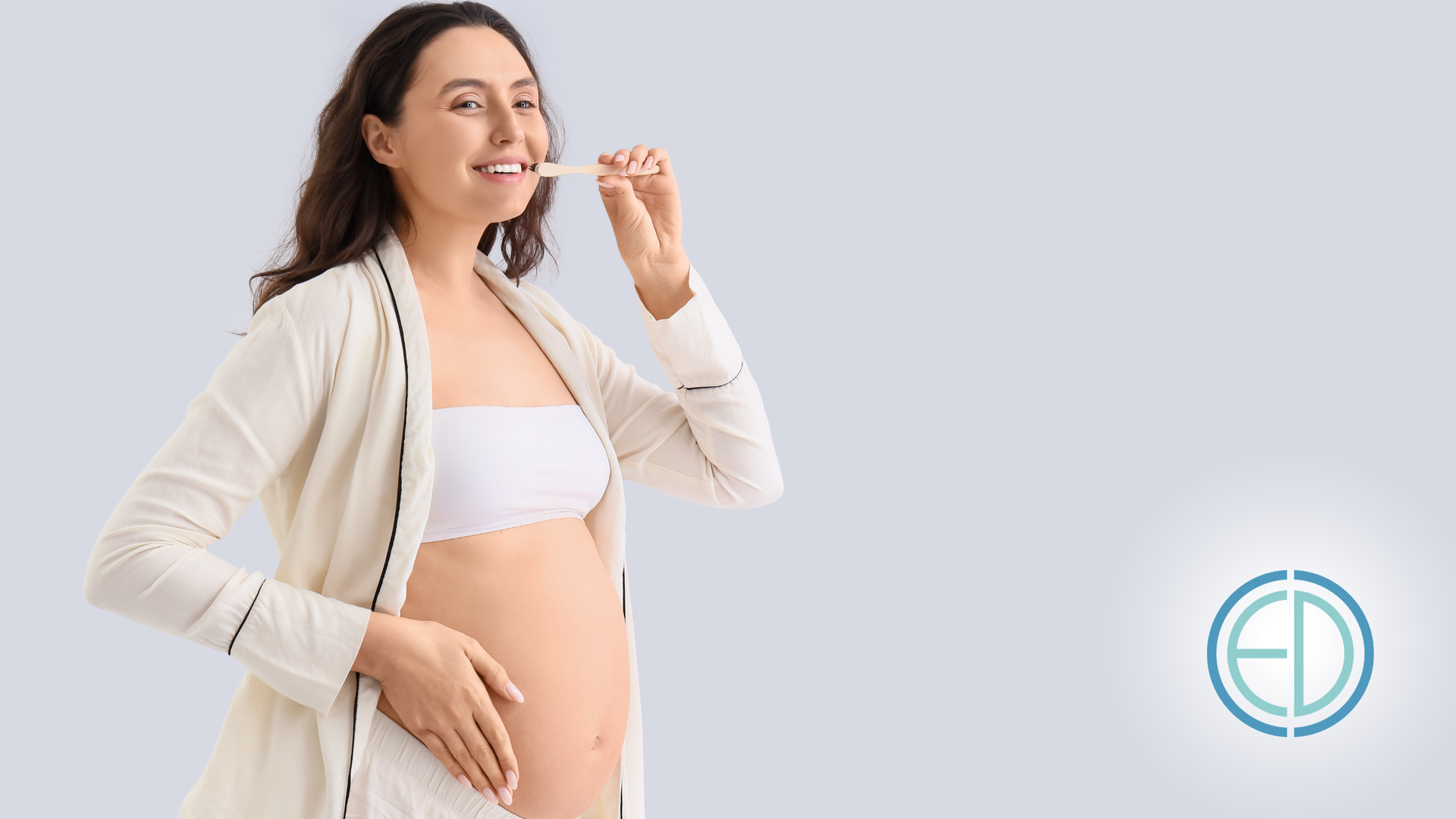 Pregnant woman smiling in a light cardigan and white top against a pale background