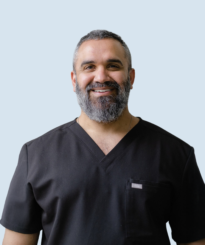 Smiling person in black medical scrubs against a light blue background
