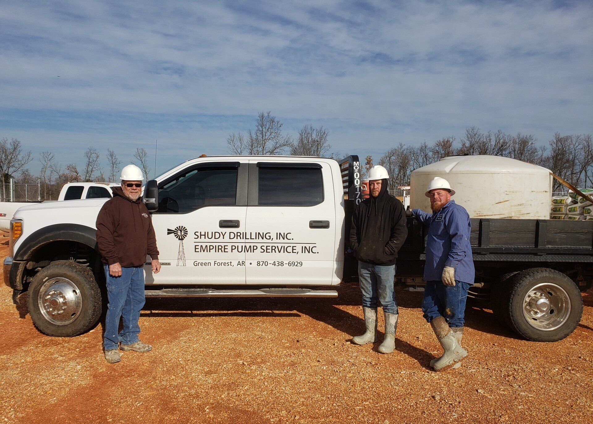 Three people in hard hats stand by a white work truck labeled