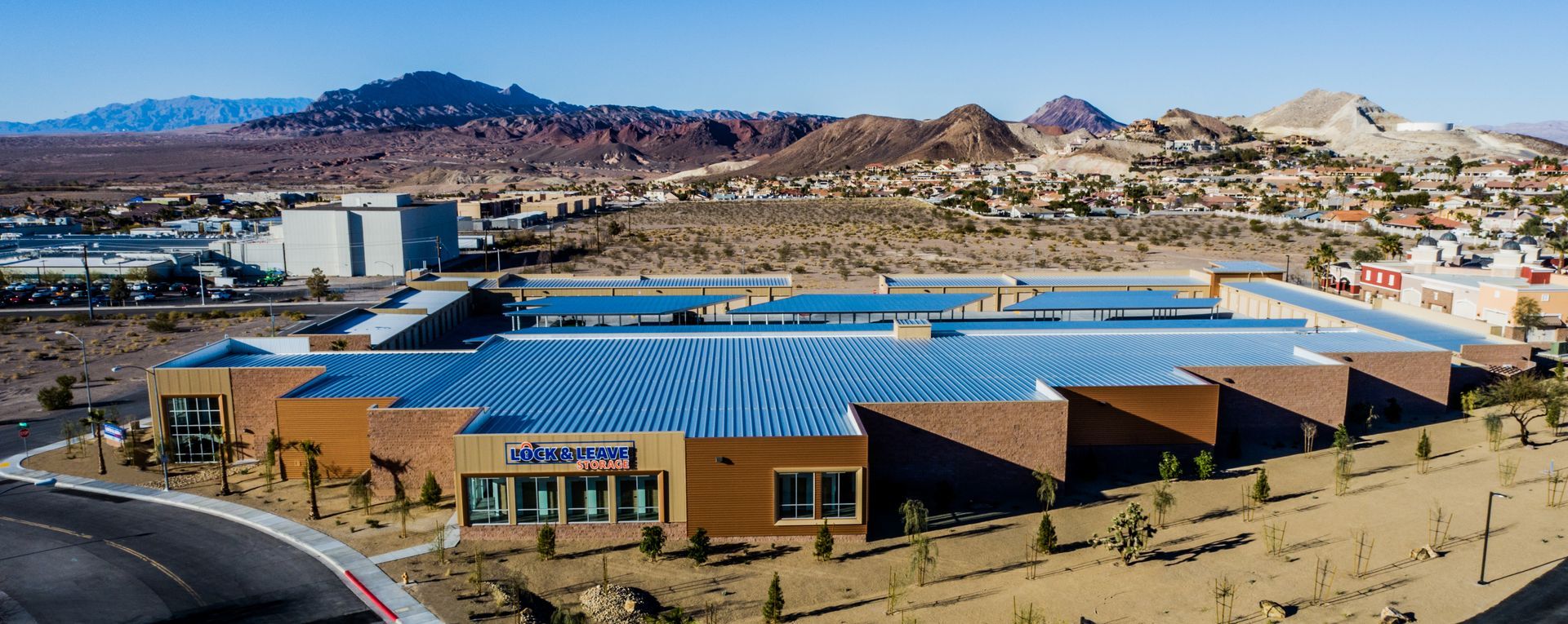 Wide aerial view of a tan building with a blue roof in a desert city with mountains behind it — commercial multi-family property photography
