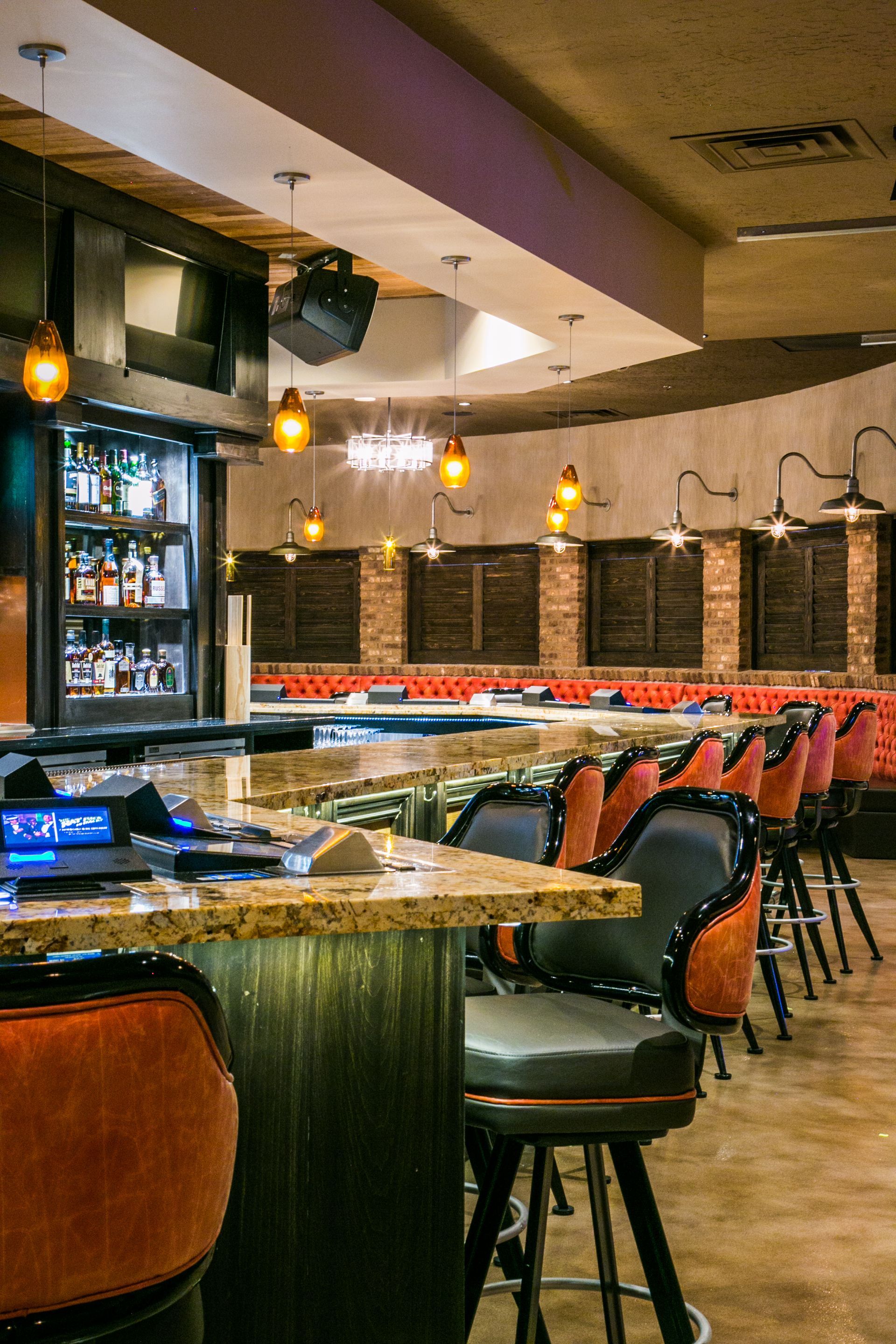 Empty bar with orange stools, hanging pendant lights, and a long counter in a warm, dimly lit interior — commercial multi-family property photography