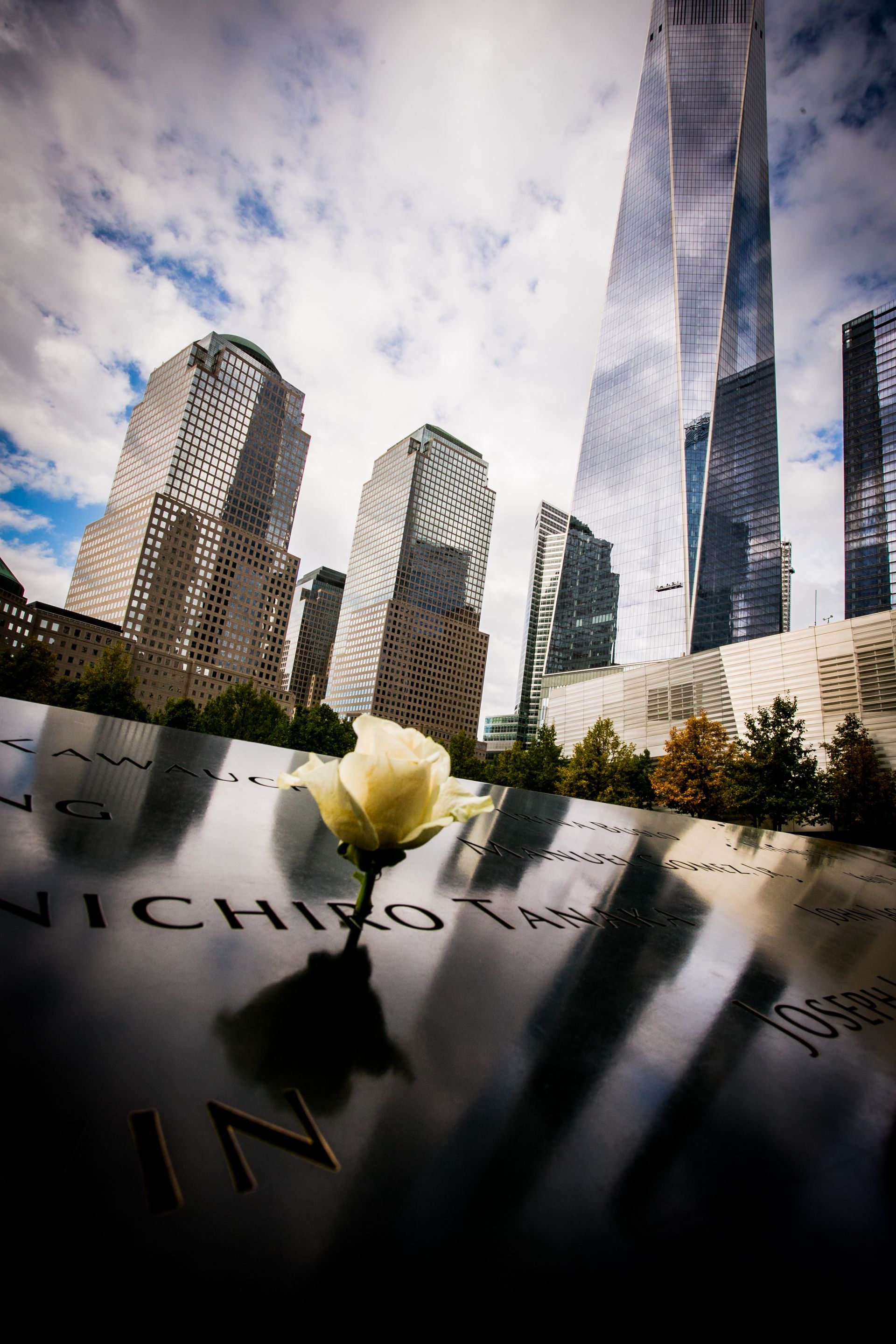 Lower Manhattan skyscrapers reflected in the 9/11 Memorial fountain with engraved names in the foreground — architectural photography