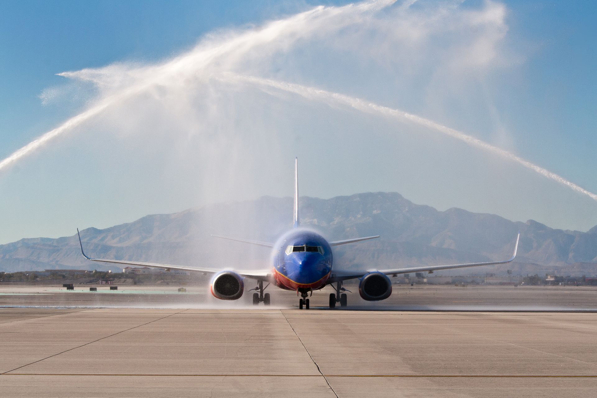 Blue airplane being sprayed with water arch at an airport runway — event photography