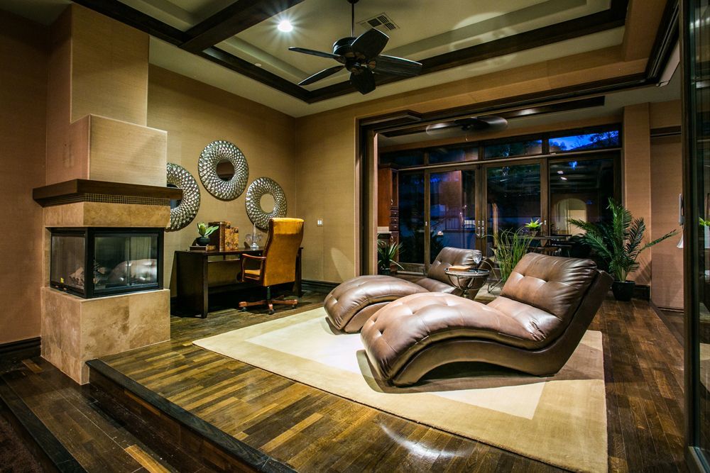 Luxurious living room with leather chaise lounge, fireplace, and large window at dusk — real estate photography