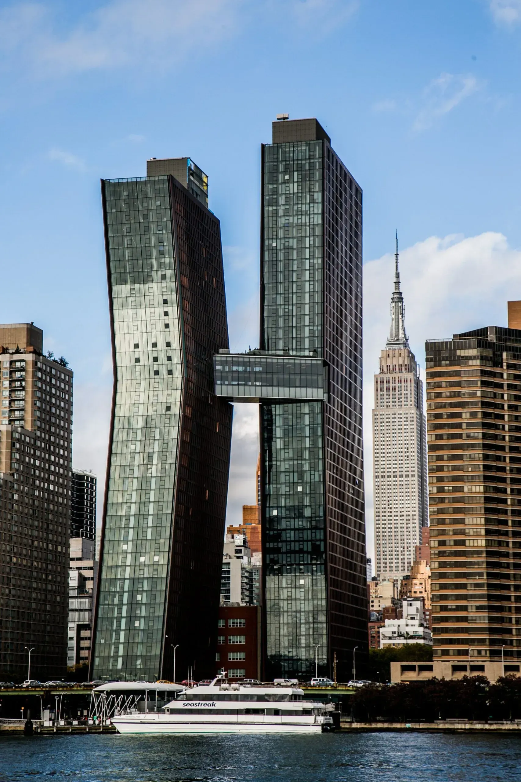 Twin glass skyscrapers by the waterfront, with a white boat below and a blue sky overhead — professional photography