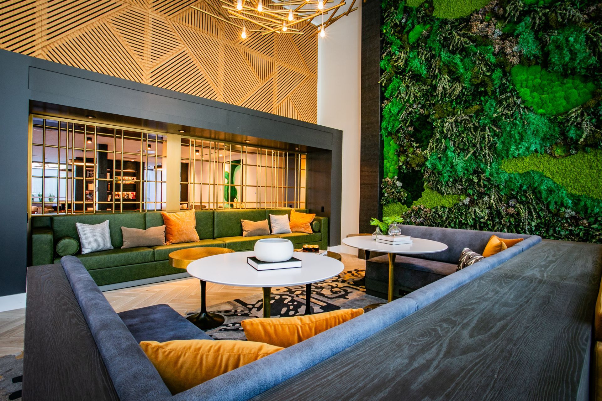 Modern lounge with gray sofas, round tables, and a green plant wall under warm lighting — commercial multi-family property photography