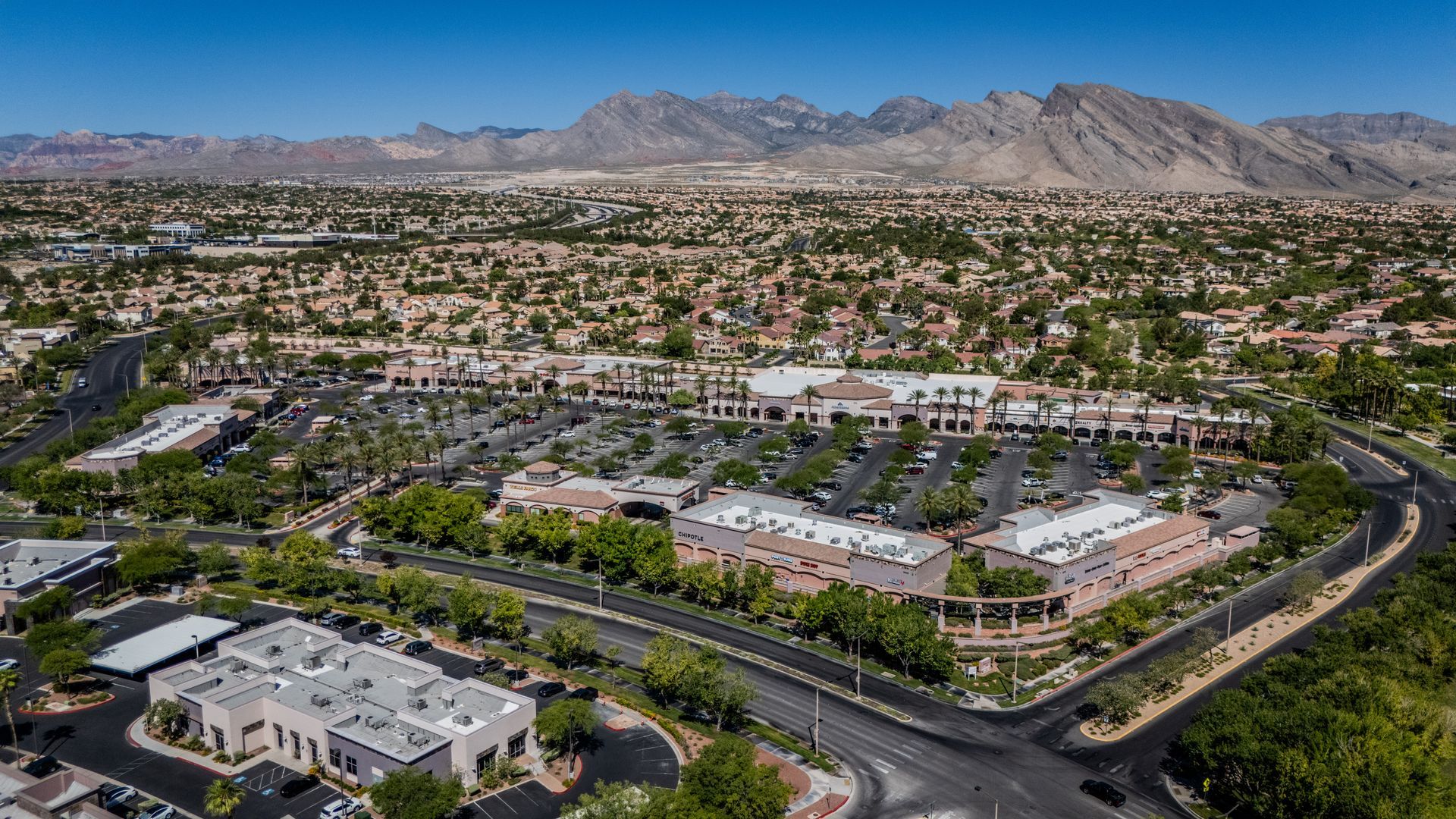 Aerial view of a suburban neighborhood with roads, houses, and mountains in the distance under a clear sky — commercial multi-family property photography