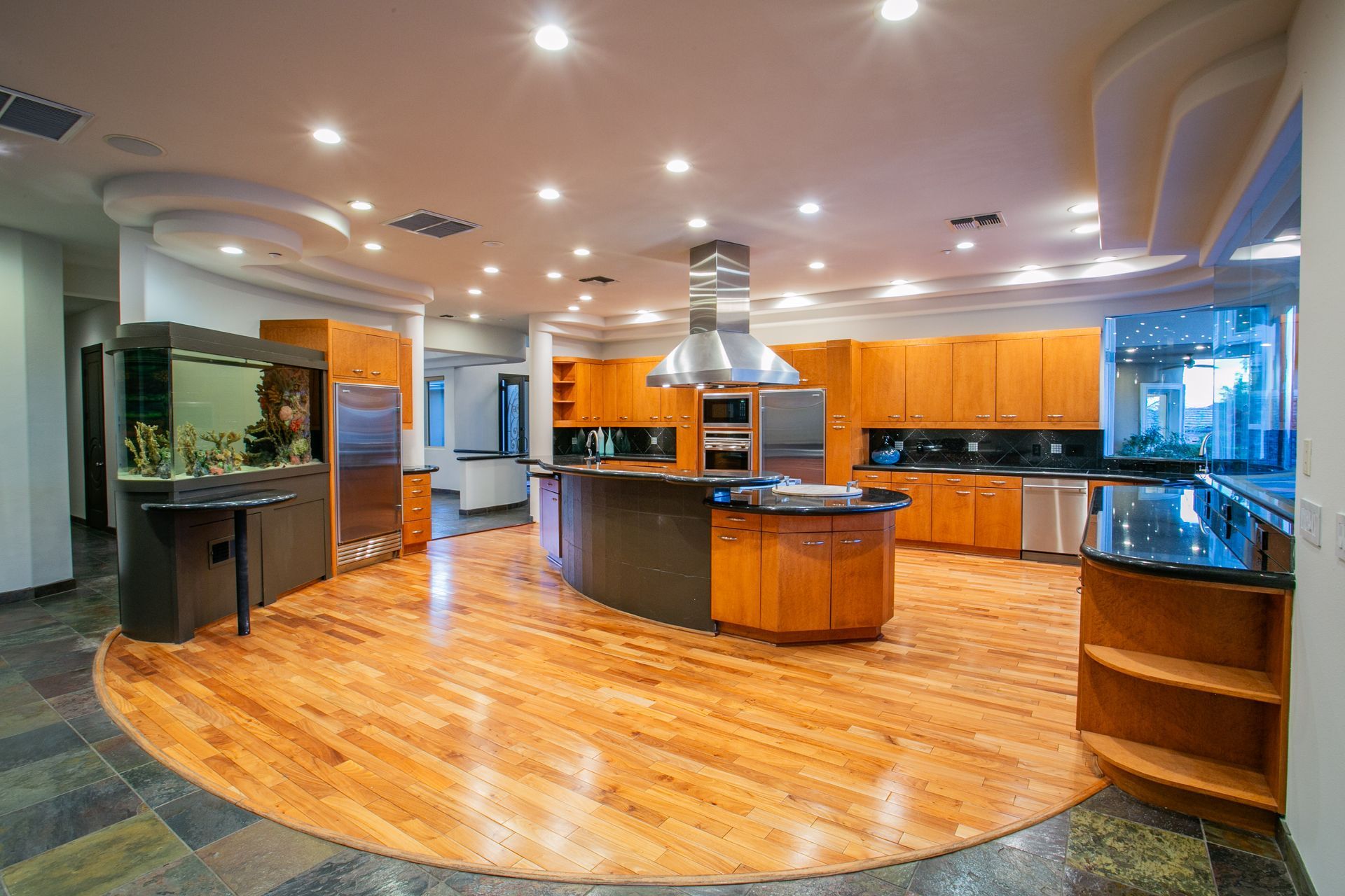 Modern kitchen with wood floors, orange cabinets, central island, and recessed lighting — real estate photography