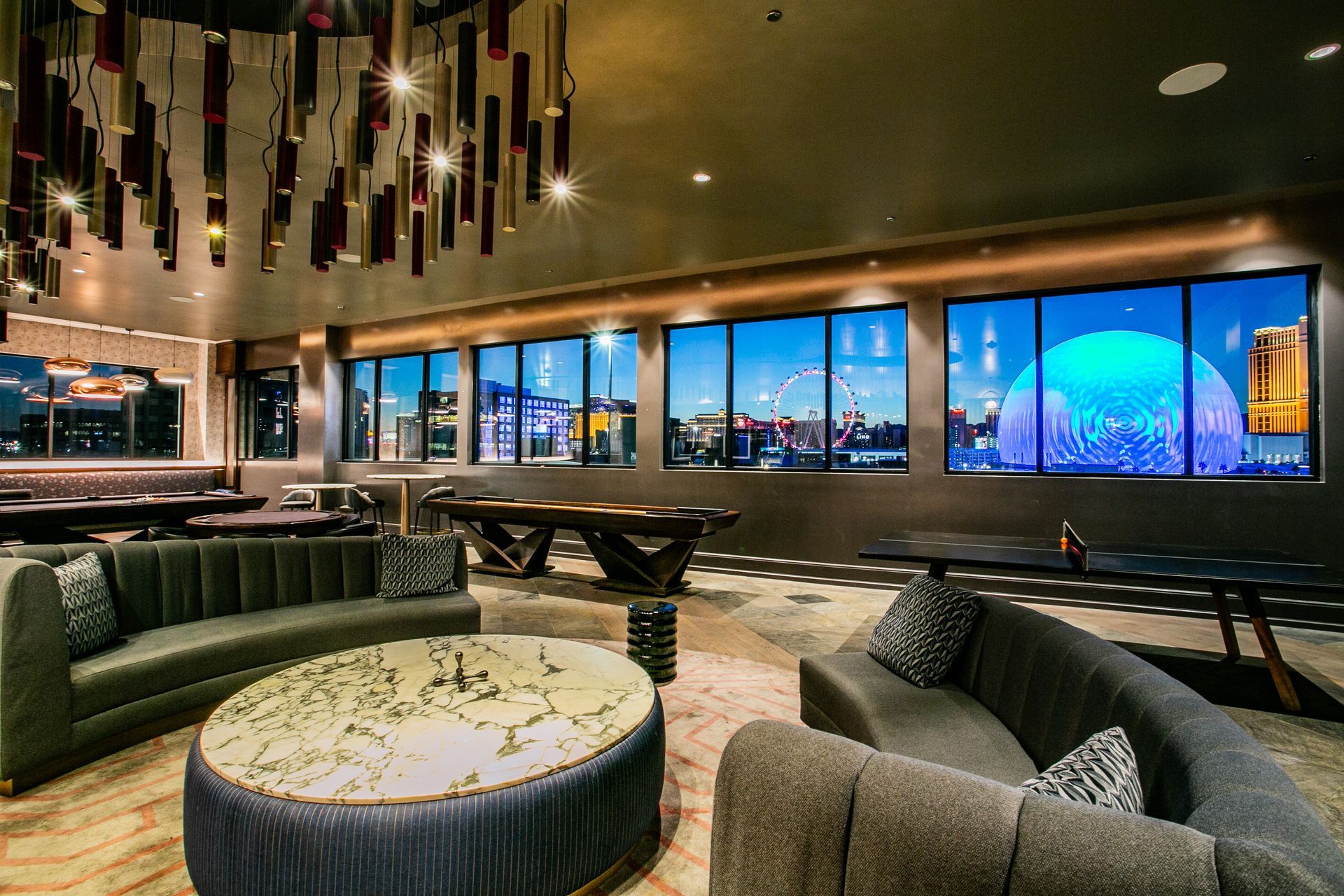 Modern lounge with curved sofas, round tables, and large windows showing a blue-lit city skyline — commercial multi-family property photography