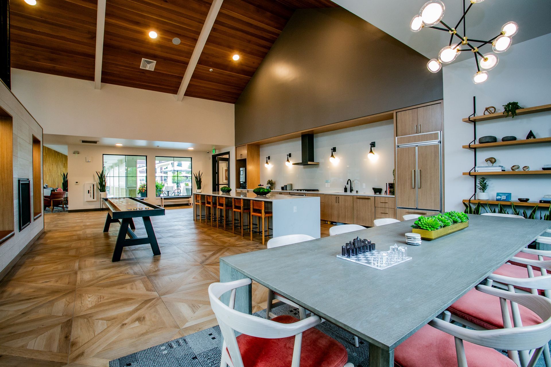 Modern open-plan kitchen and dining area with wood ceiling, long table, bar stools, and pendant lights — commercial multi-family property photography