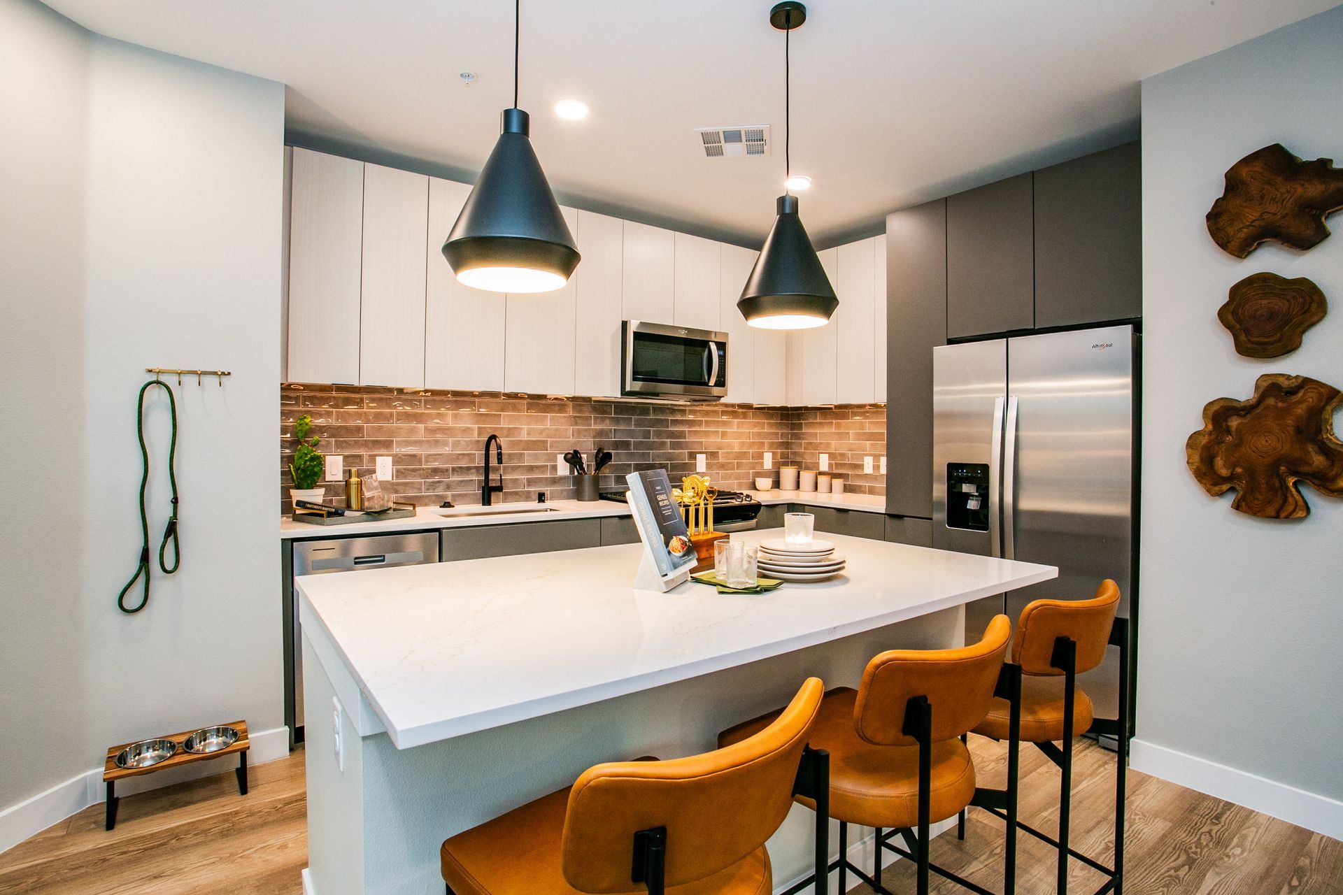 Modern kitchen with white island, orange stools, pendant lights, and stainless steel appliances — real estate photography