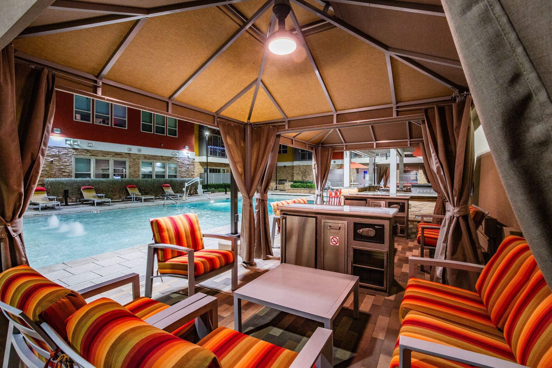 Covered poolside cabana with striped lounge chairs, table — multi-family photography