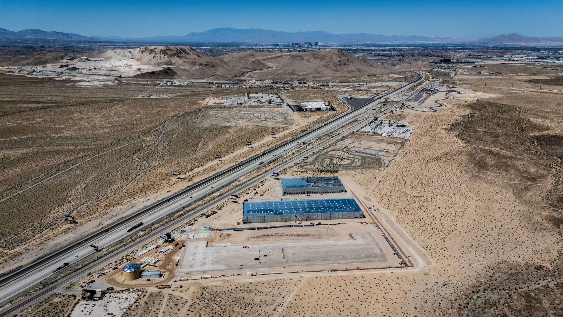 Aerial view of a desert industrial site with blue-roofed buildings beside a highway and rail line — commercial multi-family property photography