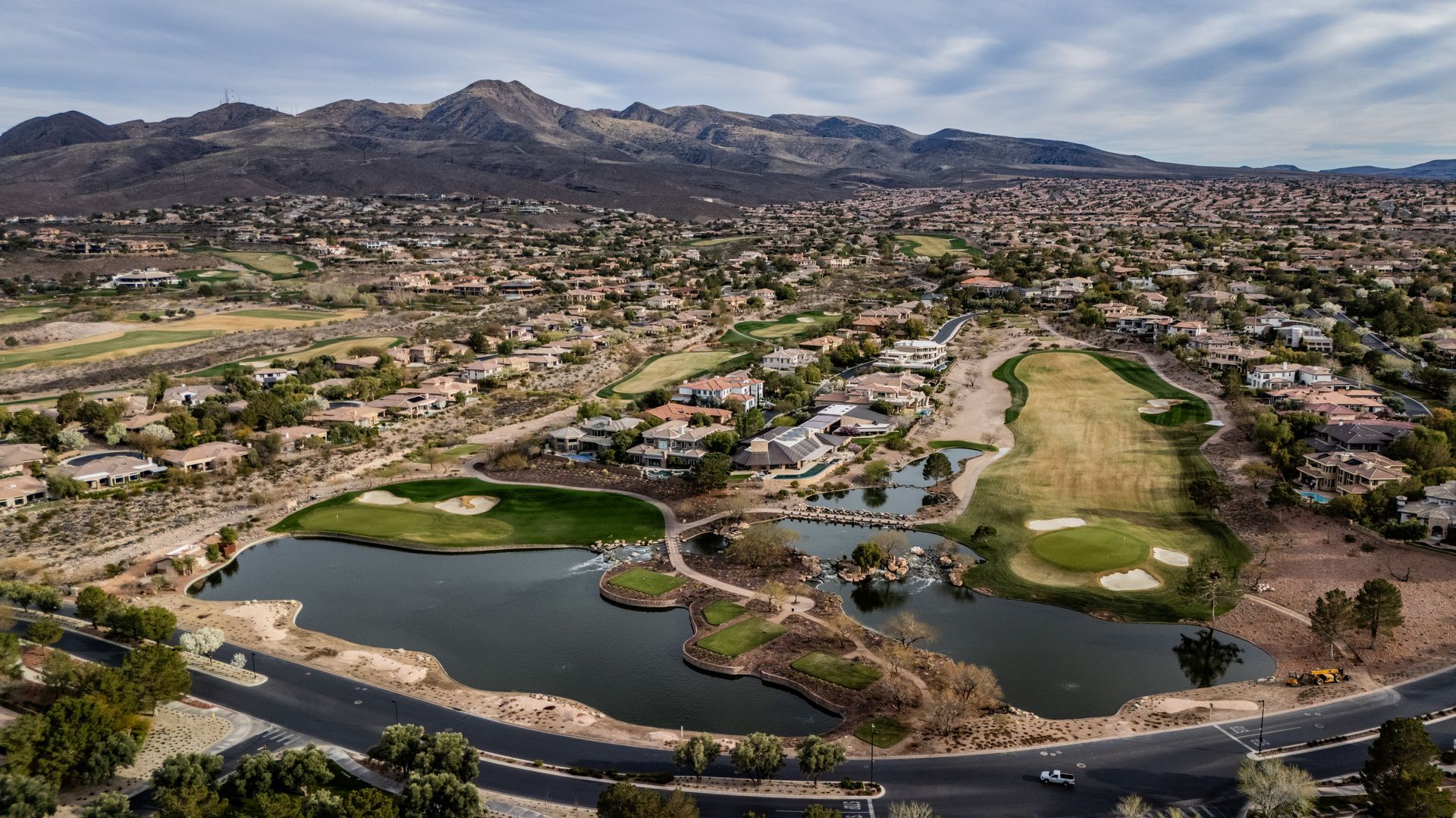 Aerial view of a suburban golf course with ponds, homes, and mountains in the background — real estate photography