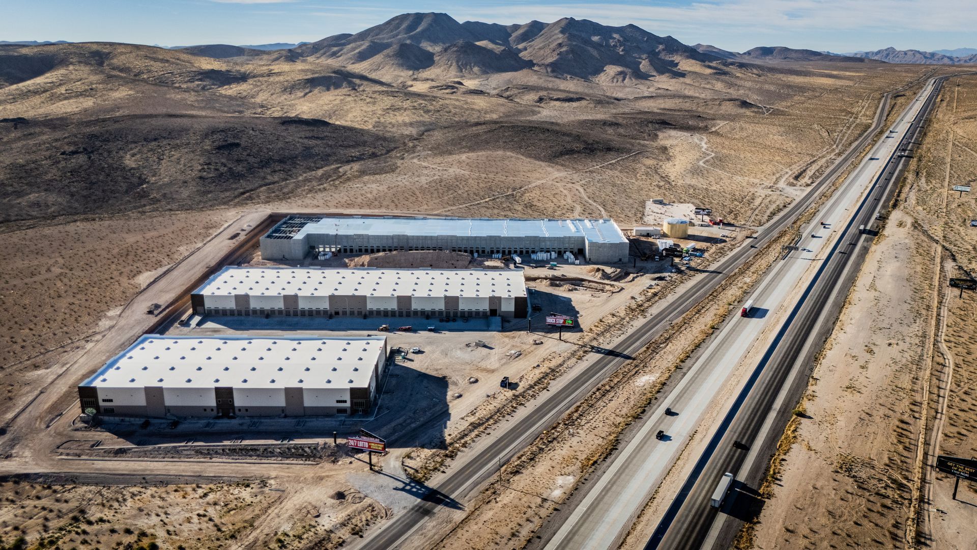 Aerial view of a desert facility beside a long rail or road line with mountains in the background — commercial multi-family property photography